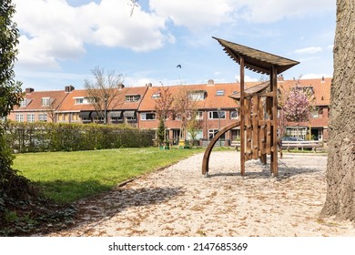 Wooden Swing Set With Climbing Equipment On A Childrens Playground With Sand In Eindhoven, The Netherlands. Friendly Rounded Construction Shapes For Kids Surrounded By Dutch Houses, Sunny Day Blue Sky