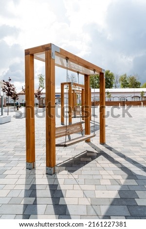 Wooden swings in the city park, a bench hanging on chains, a seat for rest, a place for walking, an art object, modern design. High quality photo