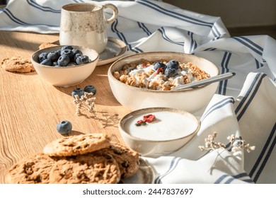 A wooden table adorned with bowls of cereal, yogurt, cookies, and blueberries, showcasing a variety of food ingredients and dishware - Powered by Shutterstock