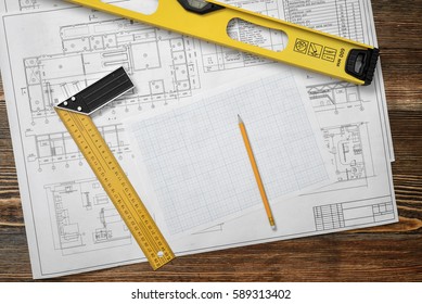 Wooden table with blueprints, a ruler with angle bar, a builders level, a pencil and cross section paper lying on it. Design and engineering. Building and construction. Professional workplace.