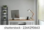 Wooden table with computer monitor and stationery and lamp in cozy home office interior decorated with green potted plants