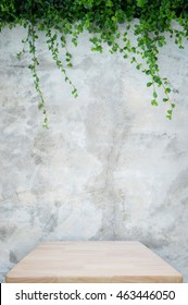 Wooden table with concrete wall and ornamental plants or ivy or garden tree for background.