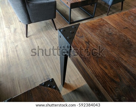 Wooden table / desk with black steel border and button pattern, and wooden bench set. The black coach sofa beside to the next. The floor is light brown wooden texture. All is in the restaurant cafe 