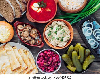Wooden table with dishes of russian cuisine - borscht, pelmeni, herring, marinated mushrooms, salted cucumbers, vinaigrette, sauerkraut, rye bread, pancakes, cheese pastry. Russian food. Top view