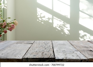 wooden table in front of the blur background with the shadow of tree flower and window