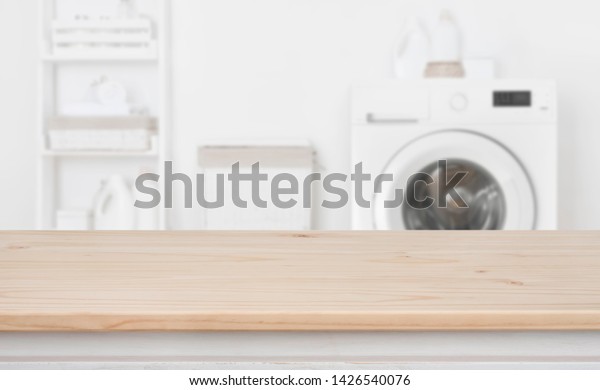 Wooden table in front of defocused washing\
machine and laundry