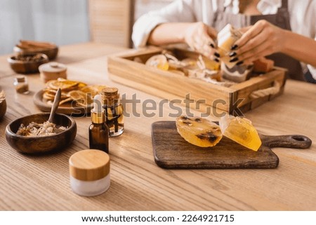 wooden table with handmade soap and natural ingredients near cropped african american craftswoman on blurred background