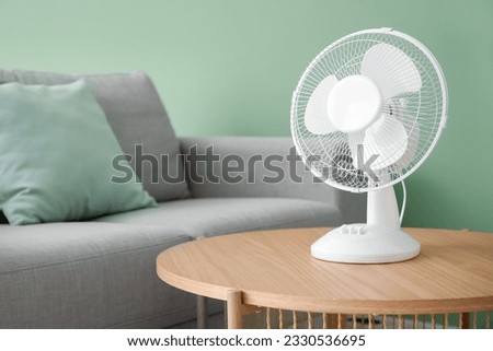 Wooden table with modern electric fan in interior of living room