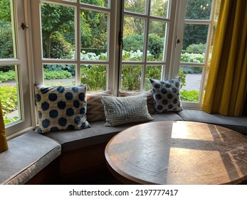 Wooden Table Near Cozy Bay Window Seat With Cushions In Room. Interior Design