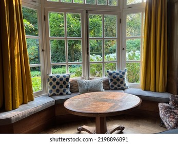 Wooden Table Near Cozy Bay Window Seat With Cushions In Room. Interior Design