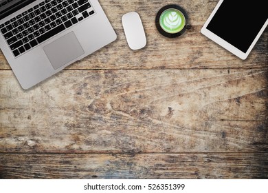 Wooden table with notepad, computer and green tea cup. View from above with copy space