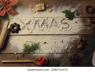  a wooden table on which flour is scattered and Christmas is written on it, and Christmas tree branches are scattered around the inscription, as well as cookies, and spoon - Powered by Shutterstock