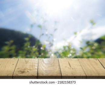 Wooden table, perspective view. Behind a blurry wooden table, a garden or a forest and the sun shines at the dawn of the day. Wooden table and beautiful blur Luxury for advertising and product