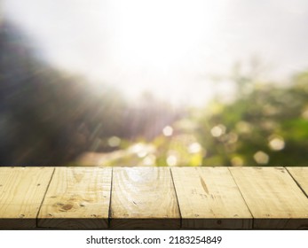 Wooden table, perspective view. Behind a blurry wooden table, a garden or a forest and the sun shines at the dawn of the day. Wooden table and beautiful blur Luxury for advertising and product