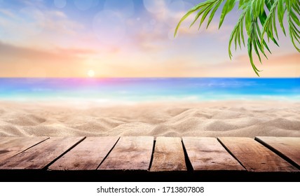 A wooden table product display with a summer vacation, holiday background of a tropical beach and blue sea at sunset with the sun on the horizon with bokeh and palm trees. - Powered by Shutterstock