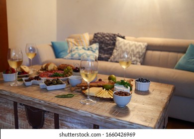 Wooden table set with white wine and assorted delicious snack of cheese and olives in living room