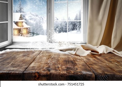 Wooden table with space for your product. Curtain in the window. Open window with snowflakes. Landscape of winter forest. Morning sunshine.