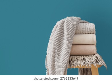 Wooden table with stack of soft blankets on blue background, closeup