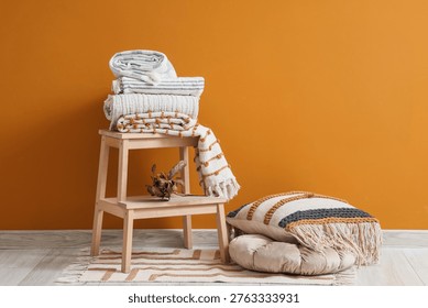 Wooden table with stack of soft blankets near orange wall