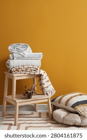 Wooden table with stack of soft blankets on orange background