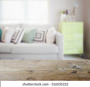 Wooden Table Top With Blur Of Geometric Pattern Pillows On Cozy Sofa And Green Sideboard In Living Room