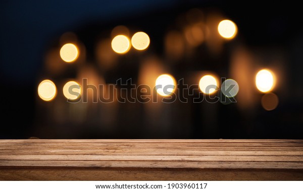 Wooden table top on blurred shop window of cafe\
with light bulb. Background for product display montage or key\
visual design.