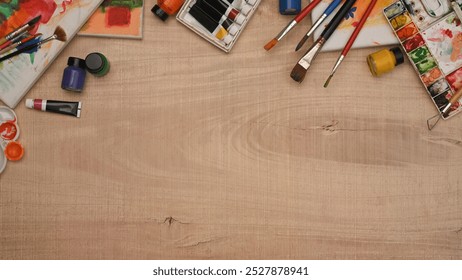 A wooden table with a variety of art supplies including paint brushes, watercolor and canvas - Powered by Shutterstock