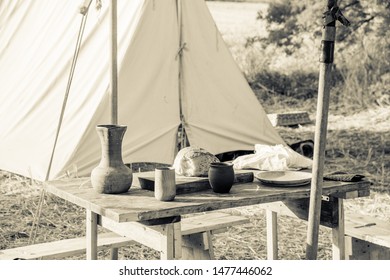 Wooden tables set up in a medieval field, visible bread, jug, glasses, wooden plates and cutting boards, vintage colors of the image.