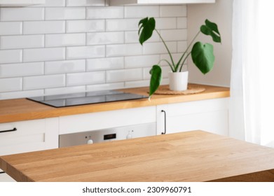 Wooden tabletop with free space for product montage or mockup against blurred white kitchen with cutting board and plant in scandinavian style in morning light - Shutterstock ID 2309960791