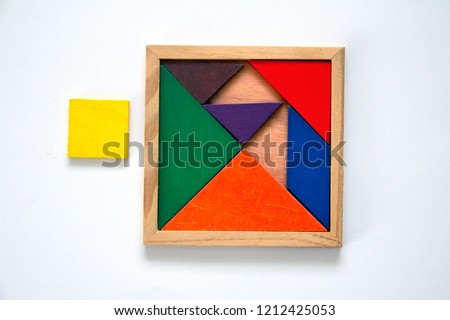 wooden tangram set in a box, misplaced. one piece is misfit, out of box, near the set.