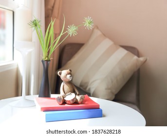 A Wooden Teddy Bear, A Red And Blue Book, A Black Vase Of Flowers, A White Candle Holder On A White Table, All Decorated In The Living Room