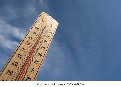 Wooden Thermometer With Red Measuring Liquid Showing High Temperature Over 32 Degrees Celsius On Background Of Blue Sky With Clouds. Concept Of Heat Wave, Warm Weather, Global Warming, Climate Change.