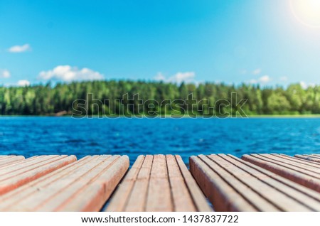 Wooden timber of a rural mooring on a lake in the middle of the forest. A peaceful river dock in the woods.Sunny footbridge. Minimal background with blue sky,clean lake and mooring in the country side