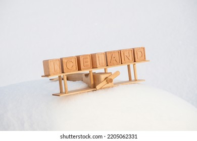 A wooden toy airplane and the country of Iceland, made up of their cubes against the background of snowy mountains. The concept of traveling to the northern countries of Europe, to Iceland