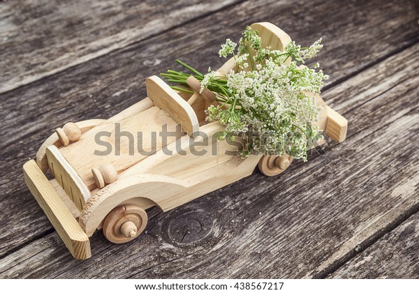 Wooden toy car with bouquet of wild\
flowers on a background of old boards. Place for text.\
