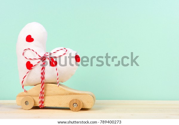 Wooden toy\
car carrying homemade heart gift against a turquoise background.\
Valentines Day or love\
concept.