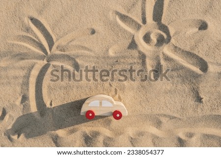 Wooden toy car on sandy beach background with painted sun and palm. Eco-friendly travel, reduce carbon footprints, environmental impact, Conscious Traveler, Environmentally Friendly, responsible
