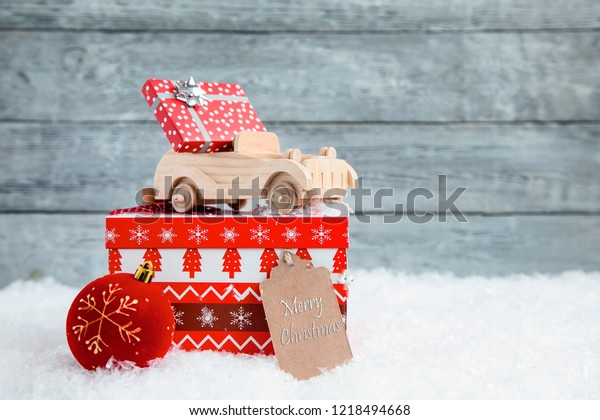 wooden toy car with a small gift on\
Red Christmas box. Concept of Christmas or New\
Year