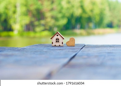 Wooden toy house next to a wooden heart, stands on a wooden table on the lake. The concept of selling, buying, renting real estate, family home, home for children, insurance, Happy life in your home, 
