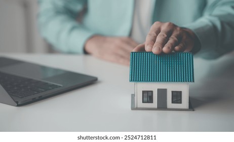 Wooden toy house protected by hand, home insurance concept, house model with real estate agent and client discussing home purchase contract, insurance or real estate loan. - Powered by Shutterstock