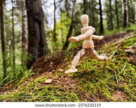 Wooden toy mannequin in forest among grass and trees in summer, autumn, spring. The concept of outdoor recreation and hiking. Healthy lifestyle. Earth Day. Save planet concept. Partial focus, blur