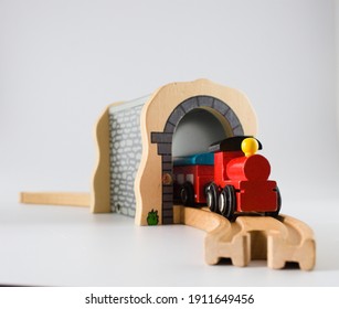 Wooden toy train coming out from the tunnel on the train tracks, isolated on white