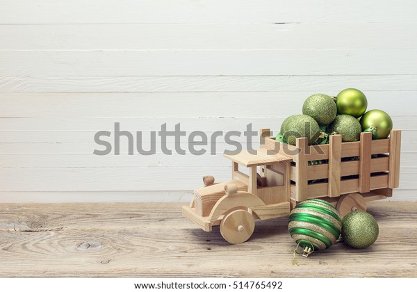 Wooden\
toy truck with a green Christmas balls in the back on white wooden\
background. Place for text. Christmas\
background.