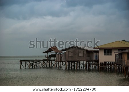 Wooden traditional native house standing on stilts by the shore and shallow waters under cloudy overcast sky