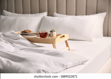 Wooden tray with breakfast and book near soft blanket on bed