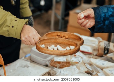 A wooden tray with cheese samples and nuts being offered at a market stall. Hands of vendor and customer interacting in a rustic food sampling scene, showcasing artisan products - Powered by Shutterstock