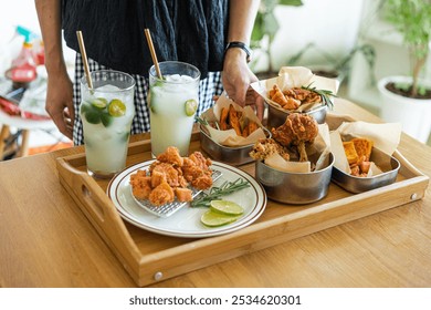 A wooden tray with crispy fried chicken, sweet potato fries, lime wedges, and refreshing drinks garnished with mint leaves. - Powered by Shutterstock