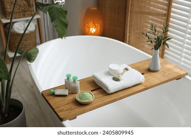 Wooden tray with spa products and green branches on bath tub in bathroom - Powered by Shutterstock