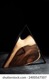 Wooden triangular wall clock on dark grey background. Luxurious accessories for home, office or restaurant made of wood and epoxy in loft style. Business style background.