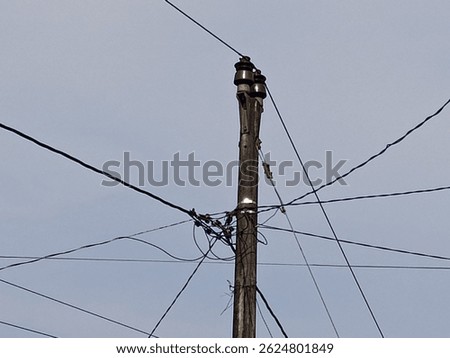 A wooden utility pole with multiple intersecting power lines against a pale sky. Electricity infrastructure in Indonesia.
